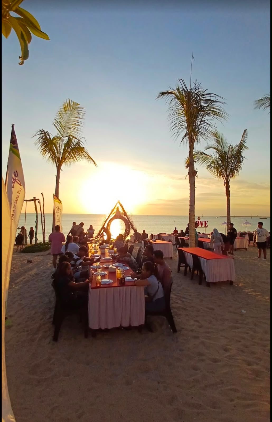 Makan malam seafood rombongan di meja panjang di Pantai Jimbaran saat matahari terbenam